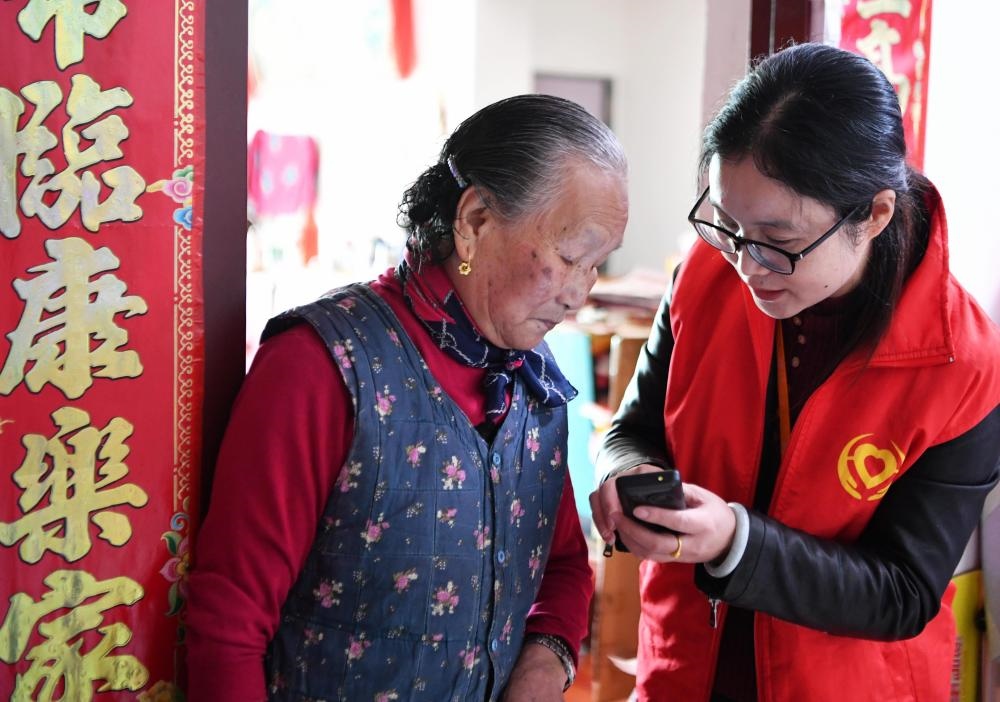 在福州市長樂區(qū)航城街道籌岐村，智慧養(yǎng)老平臺派駐社區(qū)的助老員（右）在為老人陳鳳英（左）講解養(yǎng)老定制手機的用法（2021年11月26日攝）。新華社記者 魏培全 攝