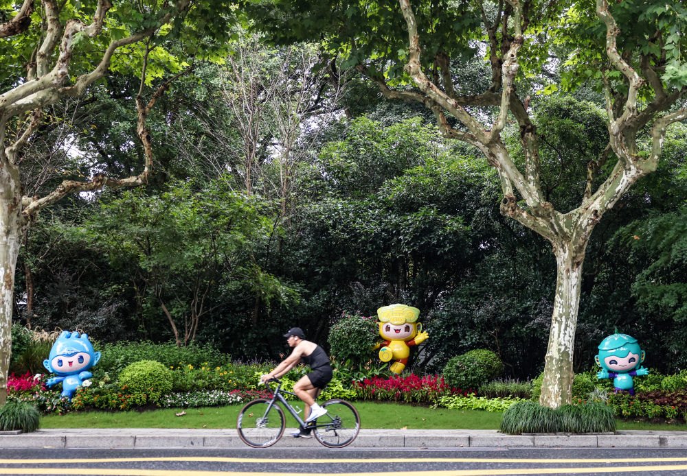 市民在杭州市南山路上一處亞運會主題吉祥物雕塑前騎自行車。