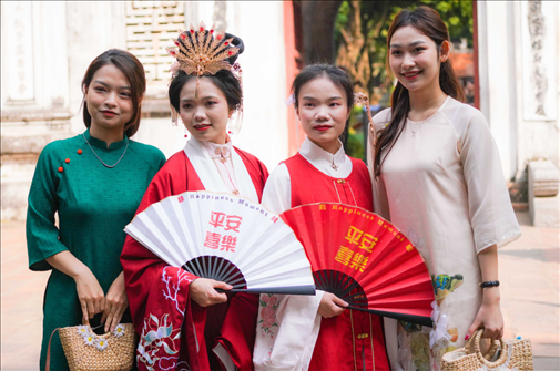 身穿古裝的中國(guó)游客和身穿越南傳統(tǒng)服飾奧黛的越南青年在文廟門前合影。