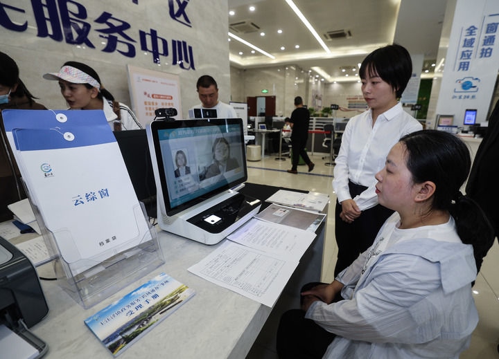 在浙江省嘉興市秀洲區(qū)王江涇鎮(zhèn)便民服務中心的“跨域通辦·云綜窗”窗口，辦理開業(yè)登記的個體工商戶（右一）通過該系統(tǒng)與江蘇省蘇州市吳江區(qū)盛澤鎮(zhèn)行政審批局工作人員視頻連線，進行身份讀取及材料線上審核（2024年5月9日攝）。新華社記者 徐昱 攝
